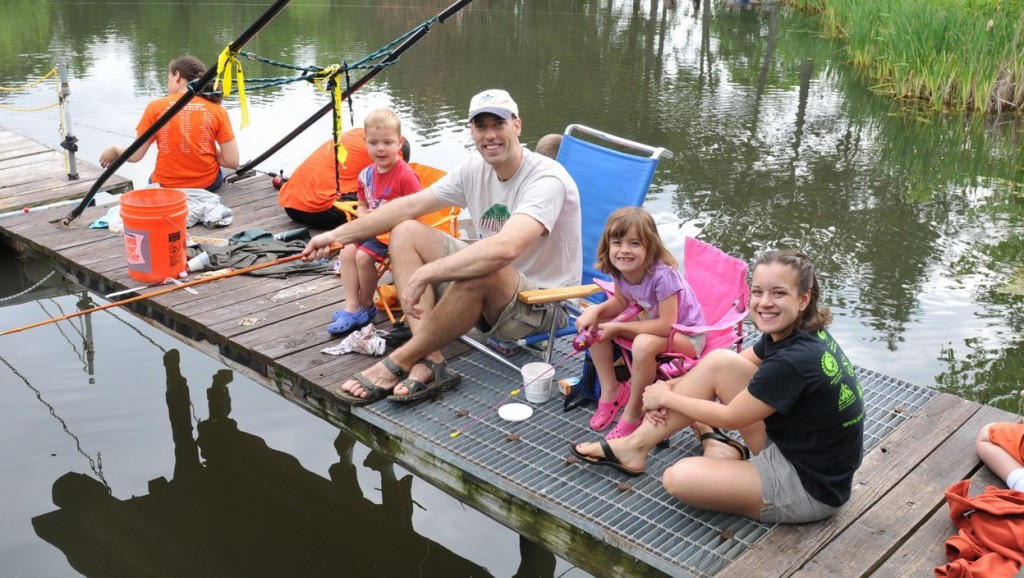 A family of four sitting on a dock smiling at the camera. They are participating in the fishing derby.