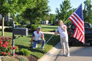 A man and a woman holding a 3 foot by 5 foot American flag installing it for the Avenue of Flags